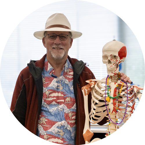 Image of Dr. Charles Lamb wearing a Hawaiian shirt, standing next to a science classroom skeleton.