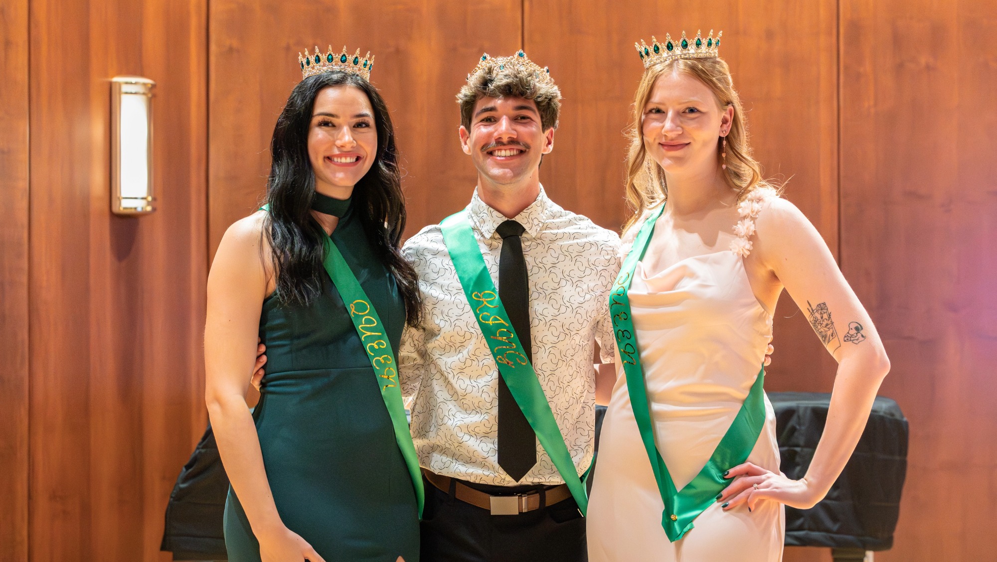 Three people with crowns and sashes smile at the camera as Swarm Days King and Queen