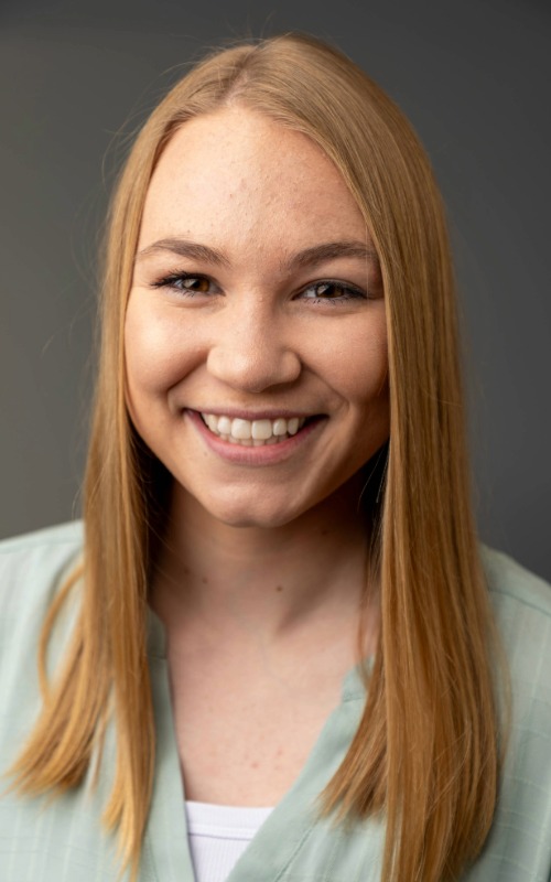 Megan Brozik A woman with blond hair and brown eyes smiles as she looks into the camera.