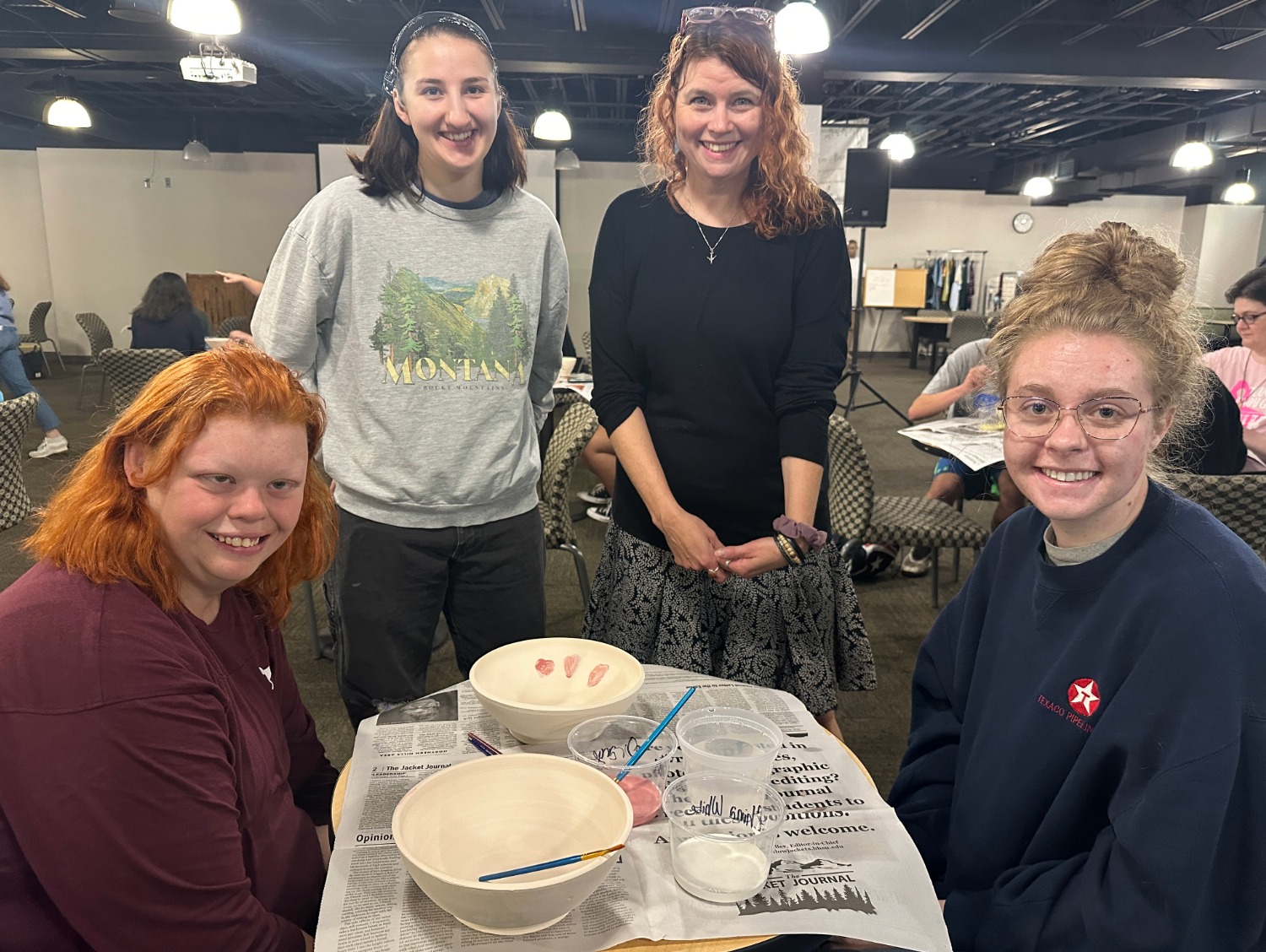 Four people smile around a table with painting supplies and ceramic bowls