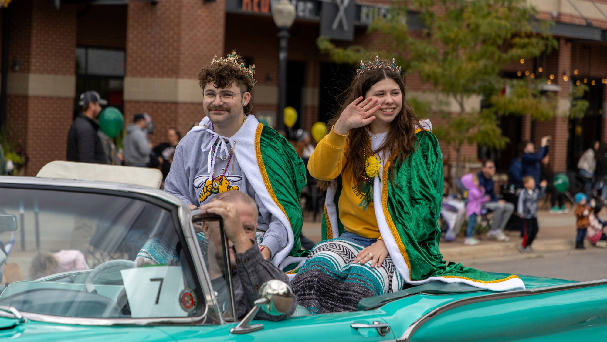 the BHSU Swarm Days King and Cave wave to the crowd while riding in a teal convertable during the annual Swarm Days parade.