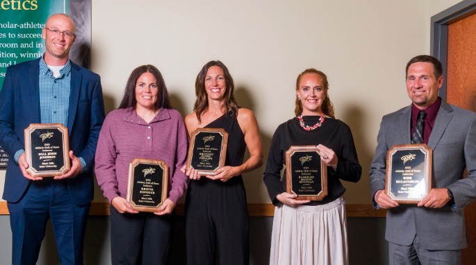 Five people smile and hold their awards as Hall of Fame inductees