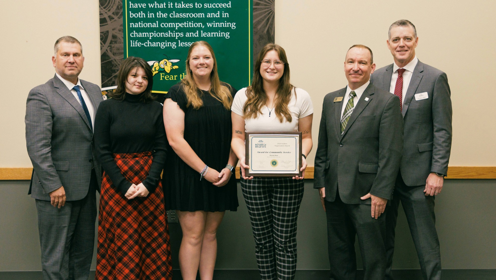 Six people smile and hold a certificate awarded to Shutter Buzz