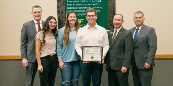 Six people smile and hold a certificate awarded to Jacket Catholic