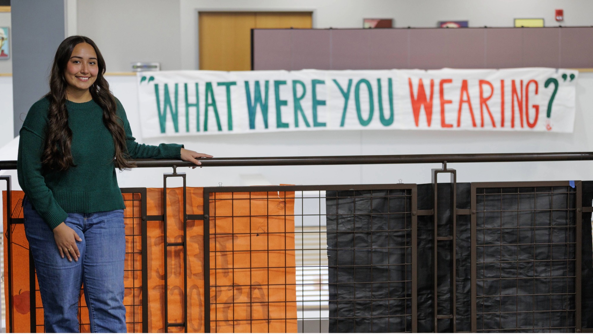 A woman with brown hair stands in front of a sign that reads 