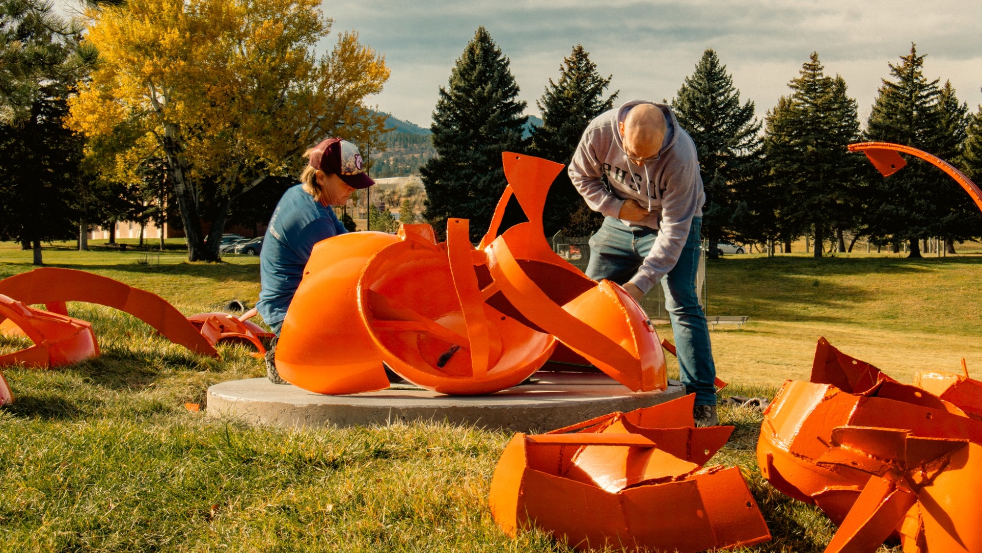 Two people work to install the orange metal pieces of a new outdoor sculpture on the BHSU campus. 