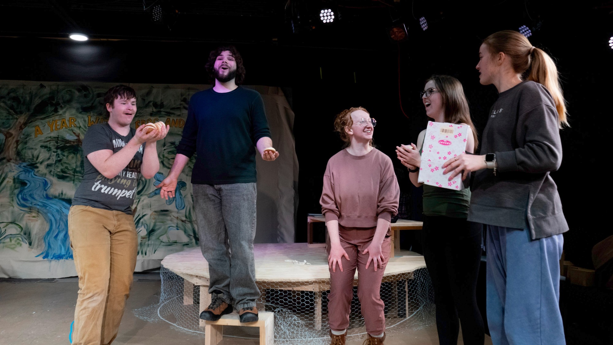 five theatre students are gathered around practicing their performance for their upcoming show