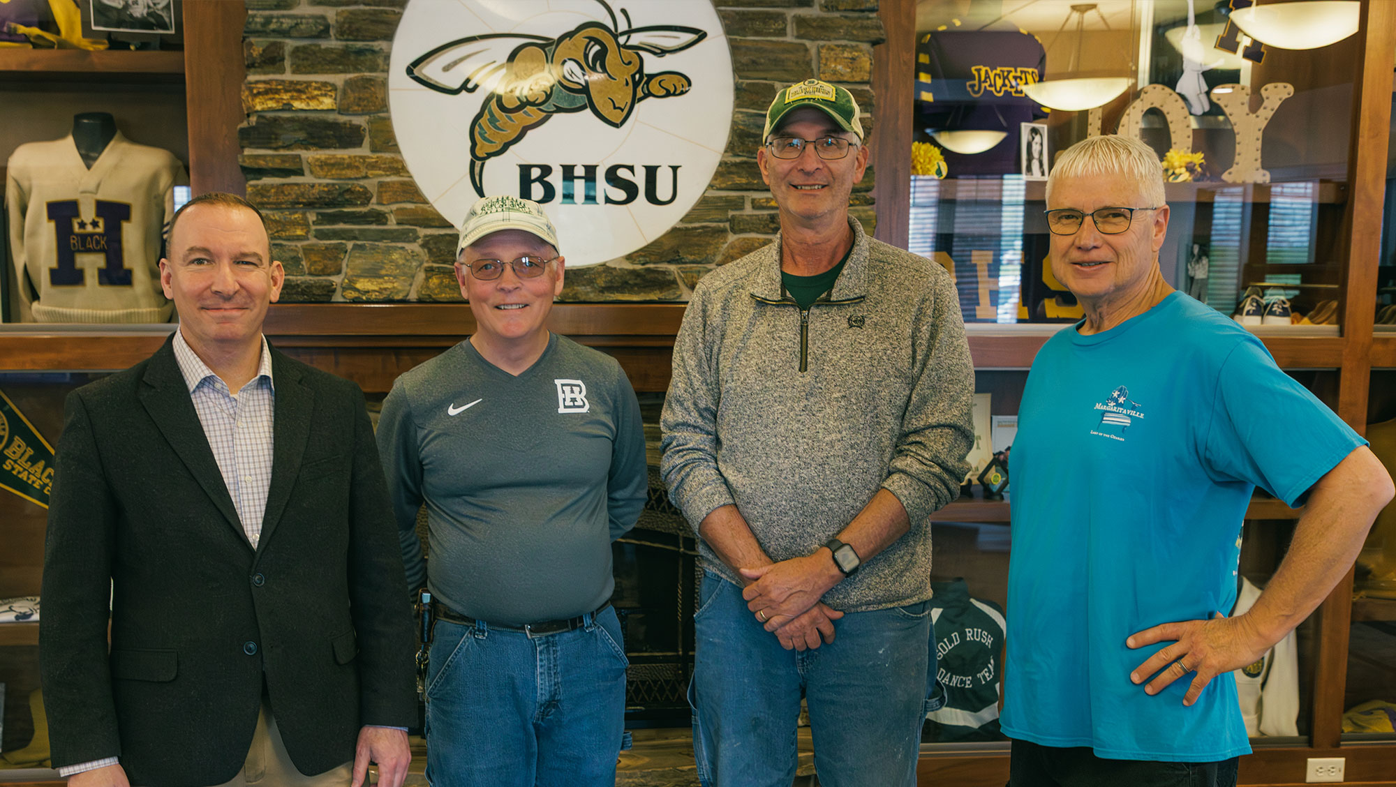 BHSU President Steve Elliott stands with three of the attending retirees at the retiree reception. They are in front of a fireplace. Mike Overby, Jeff Olstad, and Randy Culver are in the picture.