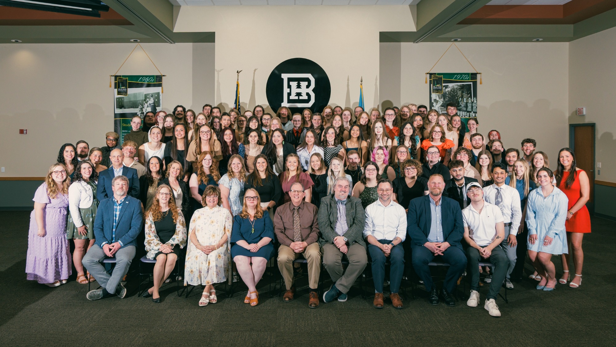 a large group of students and faculty stand on the stage for a commemorative photo of the event