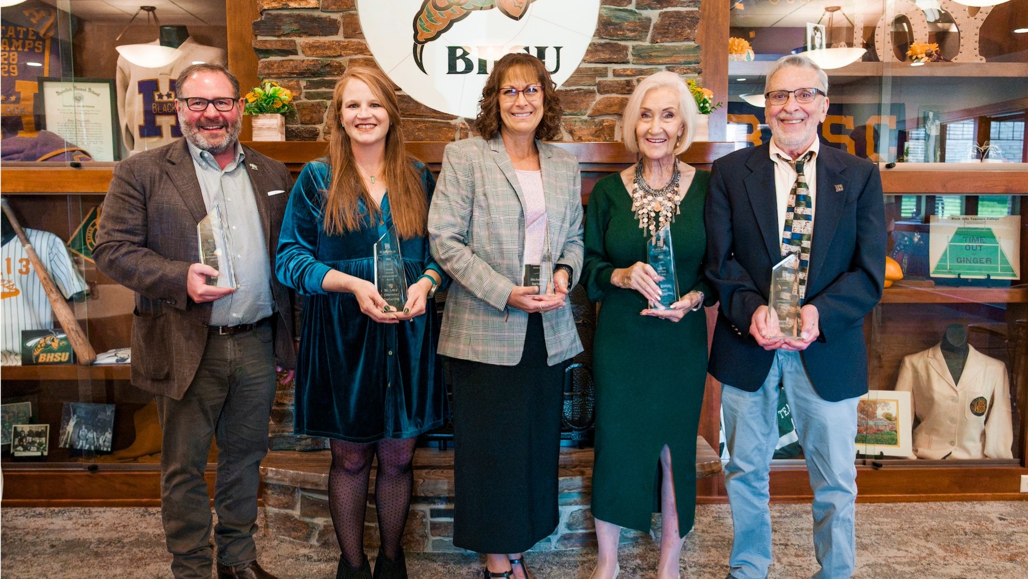 five alumni stand together for an award each holding an award that recognizes them for their accomplishments.