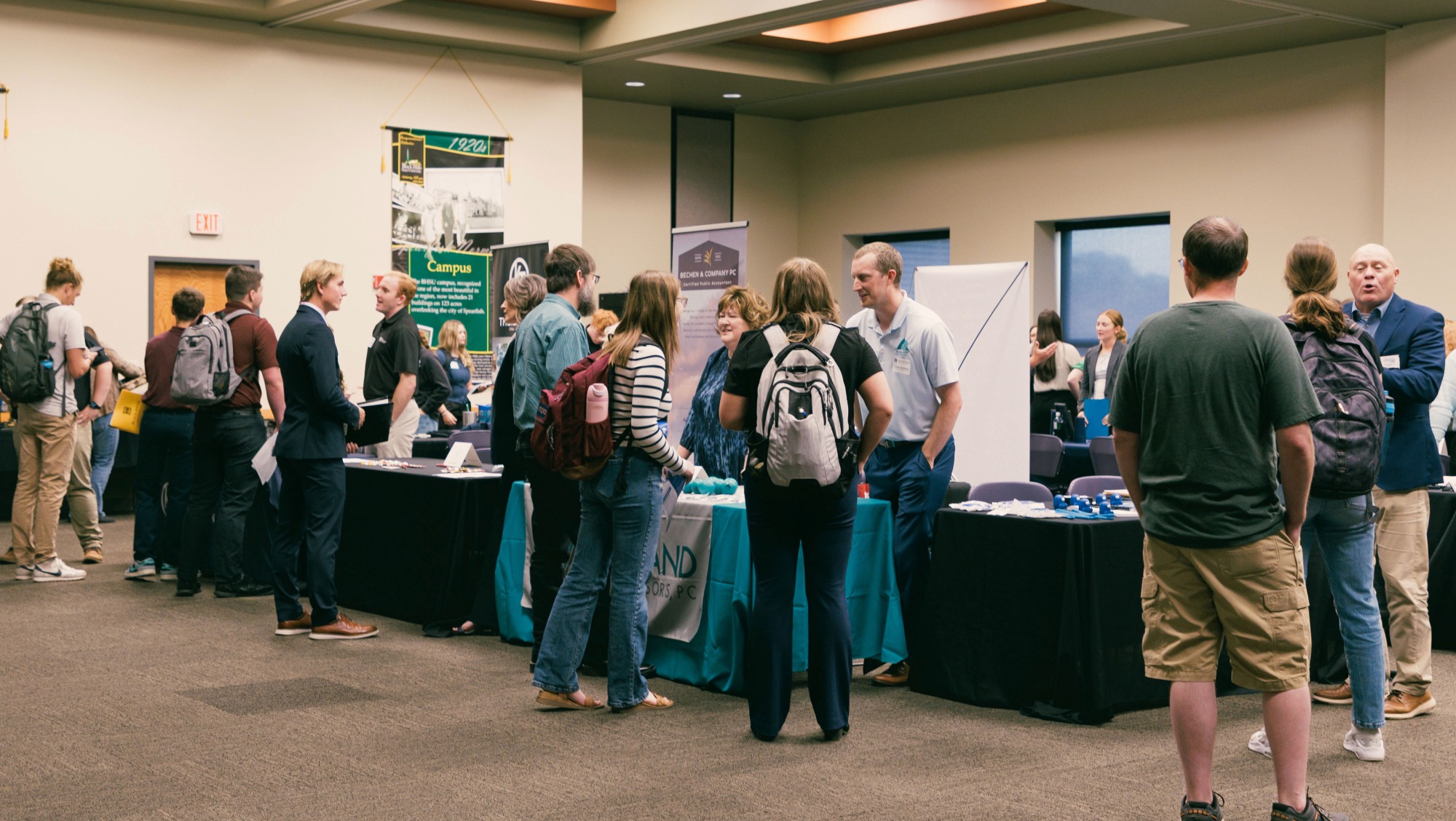 an array of booths are lined up in a room and students visit each one to learn about local businesses