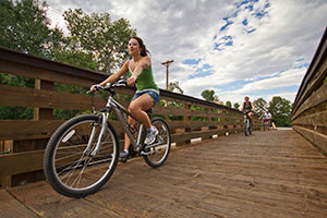 Two students ride their bikes over a bridge.