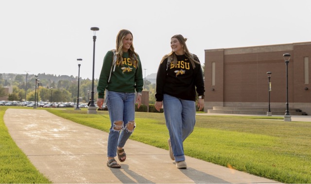 Two students walking down a pathway surrounded by grass