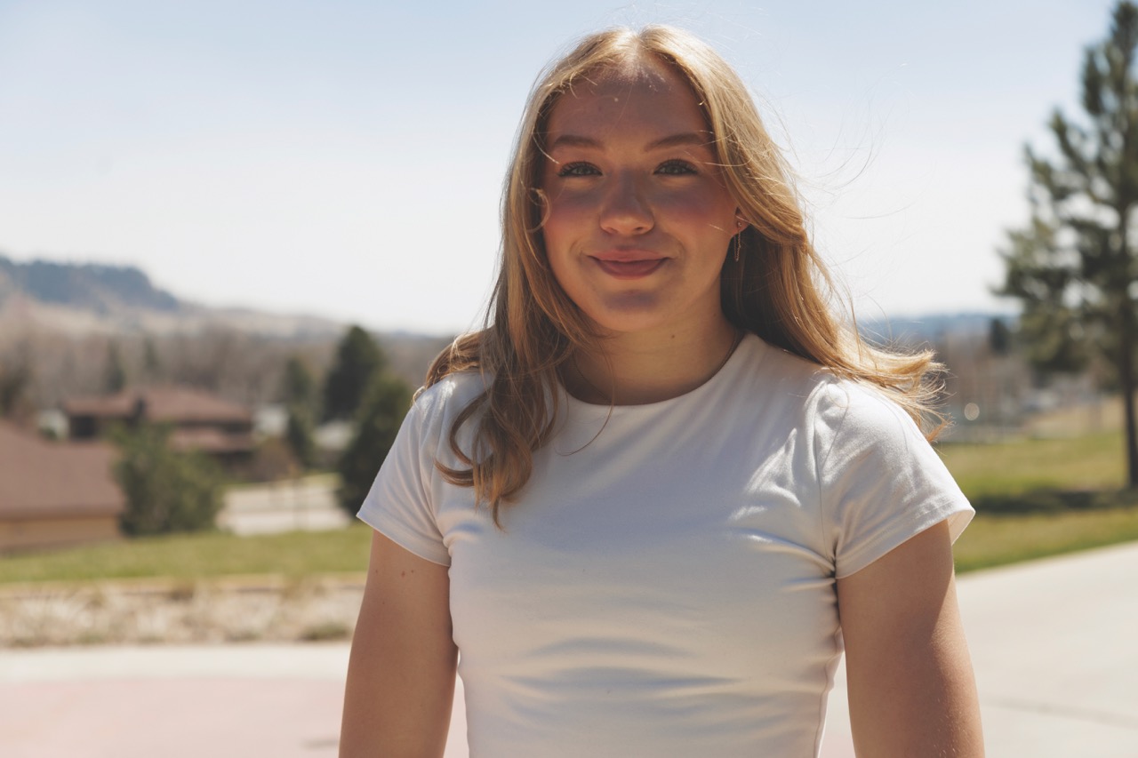 Student standing in front of landscape with hills, trees, and houses smiling. 