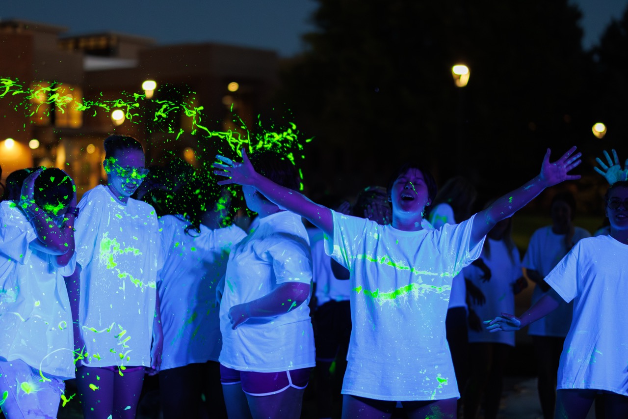 Students wearing white shirts covered in glow paint at the Green & Gold Days glow dance event.