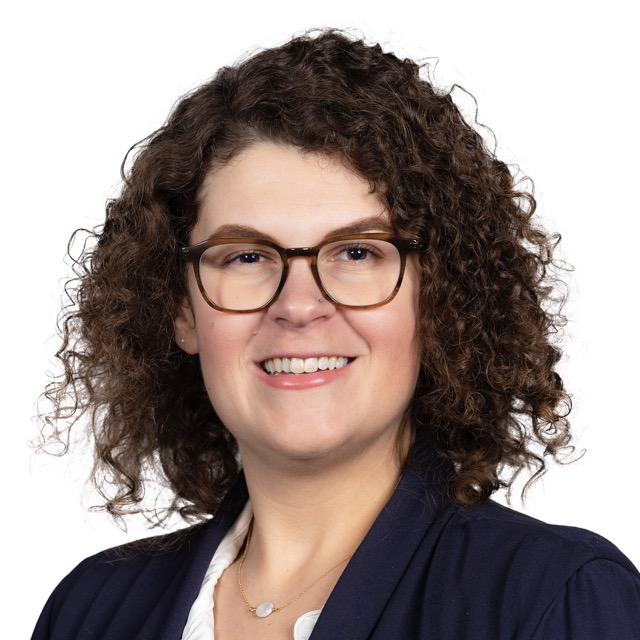 Headshot of Danielle, a smiling woman with curly hair wearing a blazer and blouse, shown from the shoulders up.
