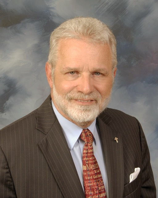 Headshot of Taylor, a smiling woman with long wavy brown hair wearing a bright blue top in front of a colorful abstract background.