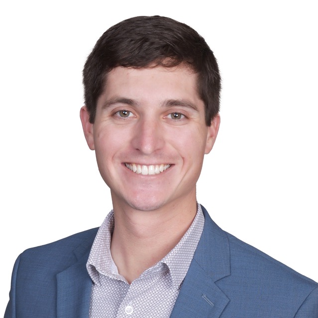 Headshot of Justin, a smiling man with short hair wearing a light blue blazer over a white shirt, posed against a simple background.