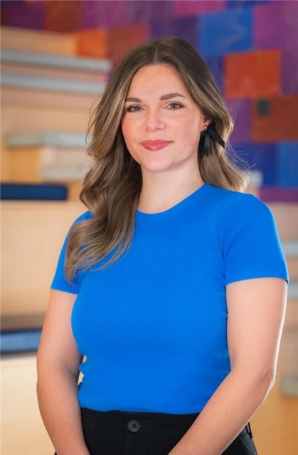 Headshot of Taylor, a smiling woman with long wavy brown hair wearing a bright blue top in front of a colorful abstract background.