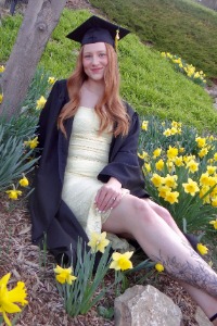 olivia-schaefers Graduate Olivia Schaefers poses in her cap and gown surrounded by yellow flowers