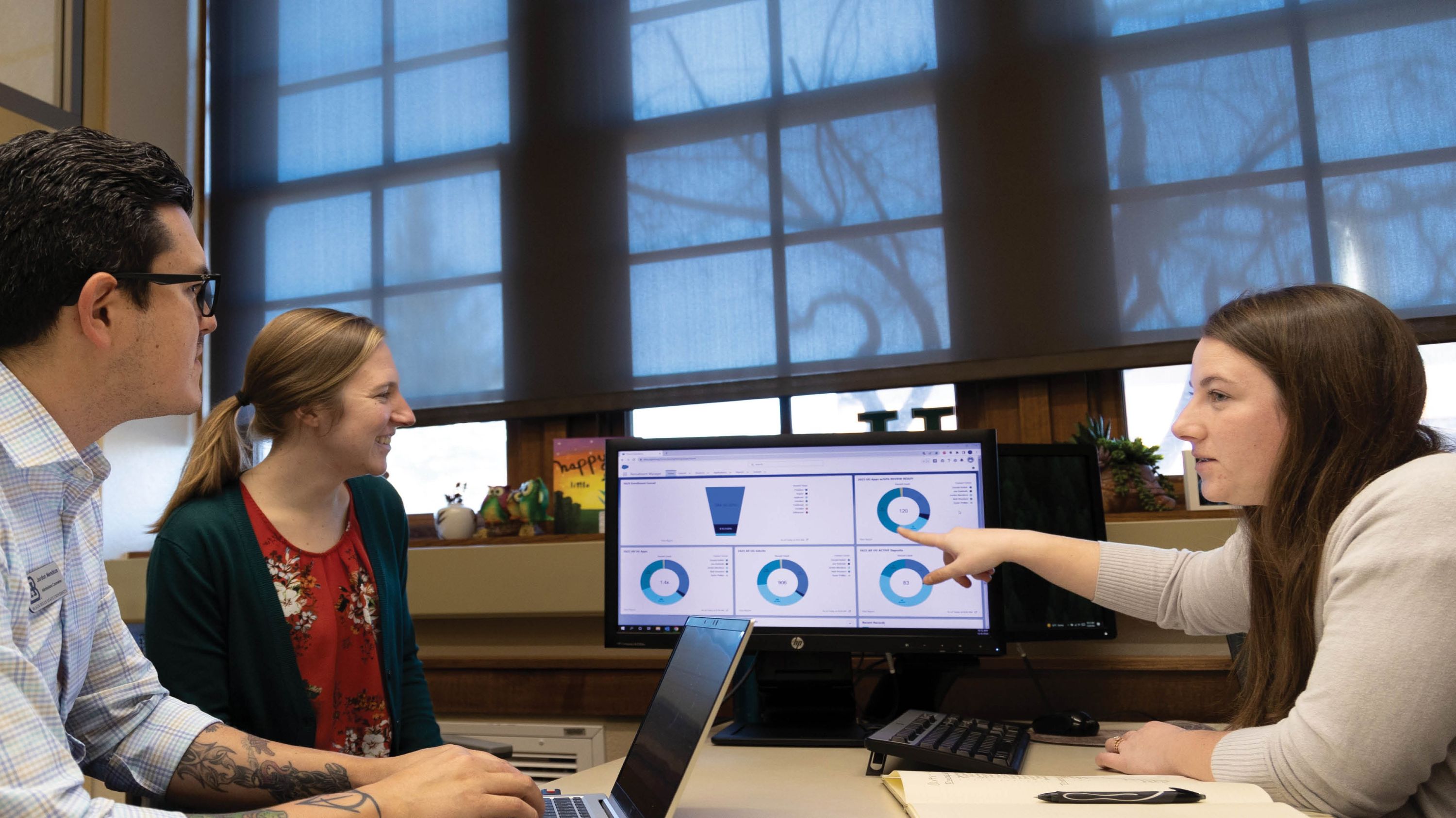 Two BHSU employees look at a computer screen while a third sits across from them, pointing at it.