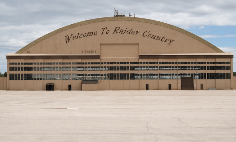 Airplane hangar at Ellsworth AFB with “Welcome To Raider Country” painted in cursive across its curved roof